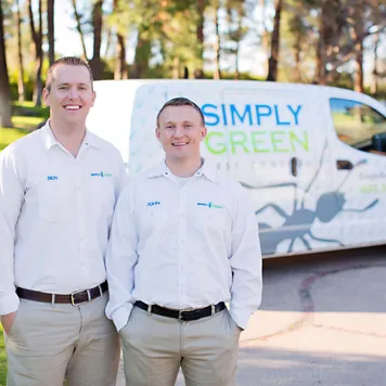 Two smiling male service workers in white uniform shirts standing in front of a branded white work van