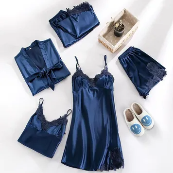 Top-down flat lay of a navy silk sleepwear set with robe, camisole, slip dress and shorts beside slippers and a small plant