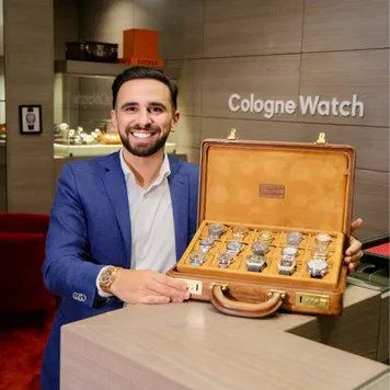 Smiling man in a blue suit presenting an open wooden briefcase full of luxury wristwatches in a watch boutique