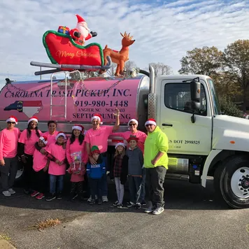 Large team of adults and children in matching pink shirts and Santa hats posing in front of a branded pink-tank truck