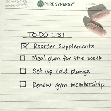 handwritten to-do list on lined notepad paper with two supplement capsules resting on the page